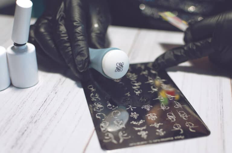 Hand pressing a nail stamper onto a painted fingernail