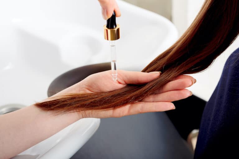 Dropper applying serum to a section of long brown hair over a salon basin