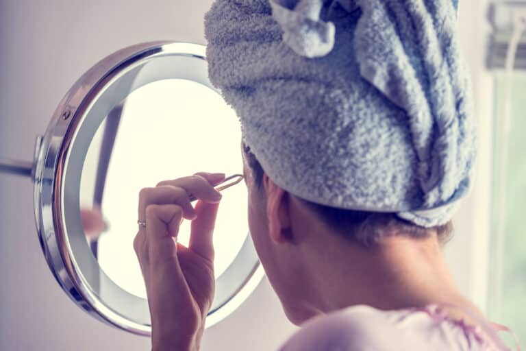 Woman Tweezing Eyebrows In Front Of Mirror