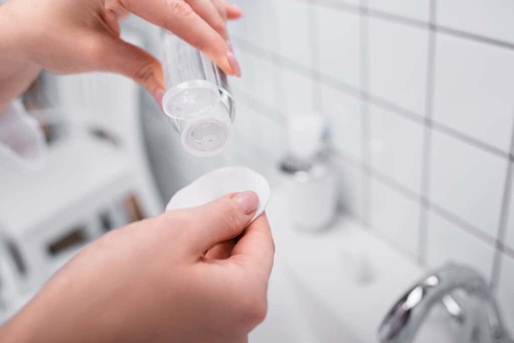 Polyhydroxy Acid (PHA) Toner (Complete Guide + The Best To Buy) - Beautygab Partial view of woman holding bottle with toner and cotton pad in bathroom