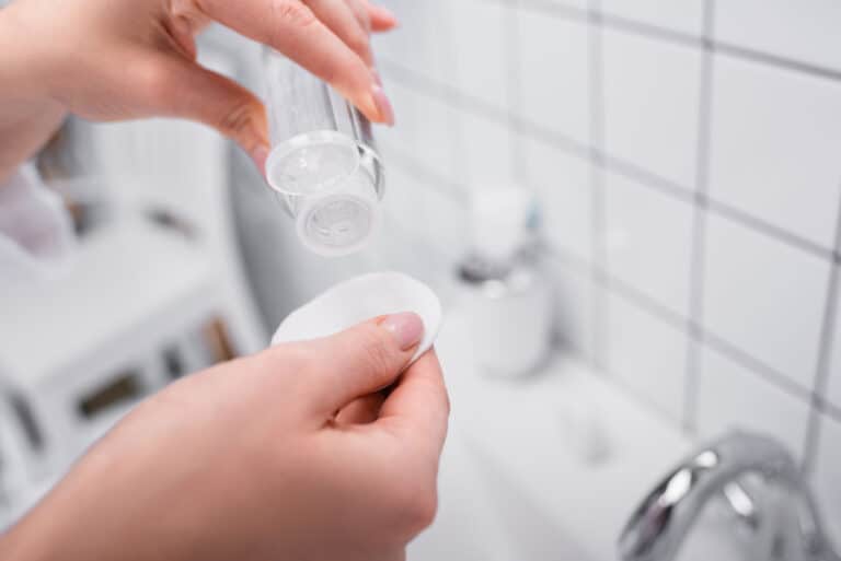 Partial view of woman holding bottle with toner and cotton pad in bathroom