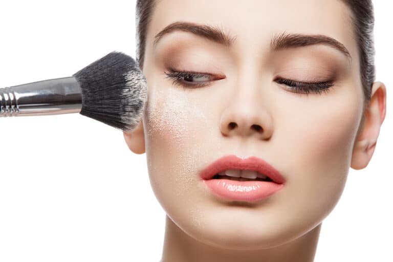 Beautiful young woman applying loose face powder with brush. Macro shot. Isolated over white background. Copy space.