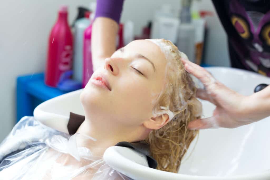 Best Castor Oil Shampoos and Conditioners - Beautygab Client leaning back into a salon basin while a stylist works conditioner through her wet hair